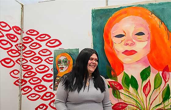 艾丽莎站在一幅色彩鲜艳的画前，画的是一个橙色头发的女人, laughing and turning her face to the left