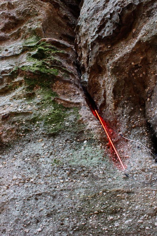 A straight red neon line traces the negative space along a wall of rock. 
