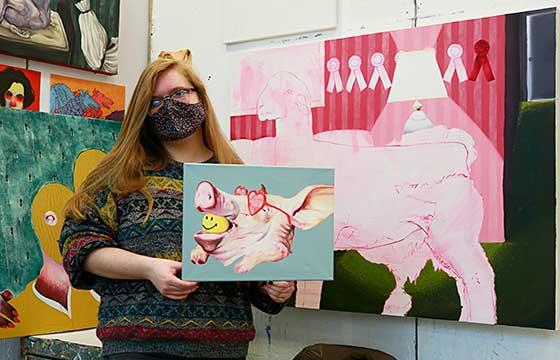 佩姬站在画室里，拿着一幅更小的粉红色的画在绿松石上